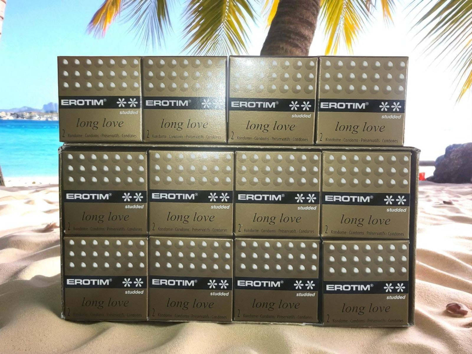 Multiple boxes of EROTIM 'long love' products stacked on a beach with palm trees and ocean in the background.